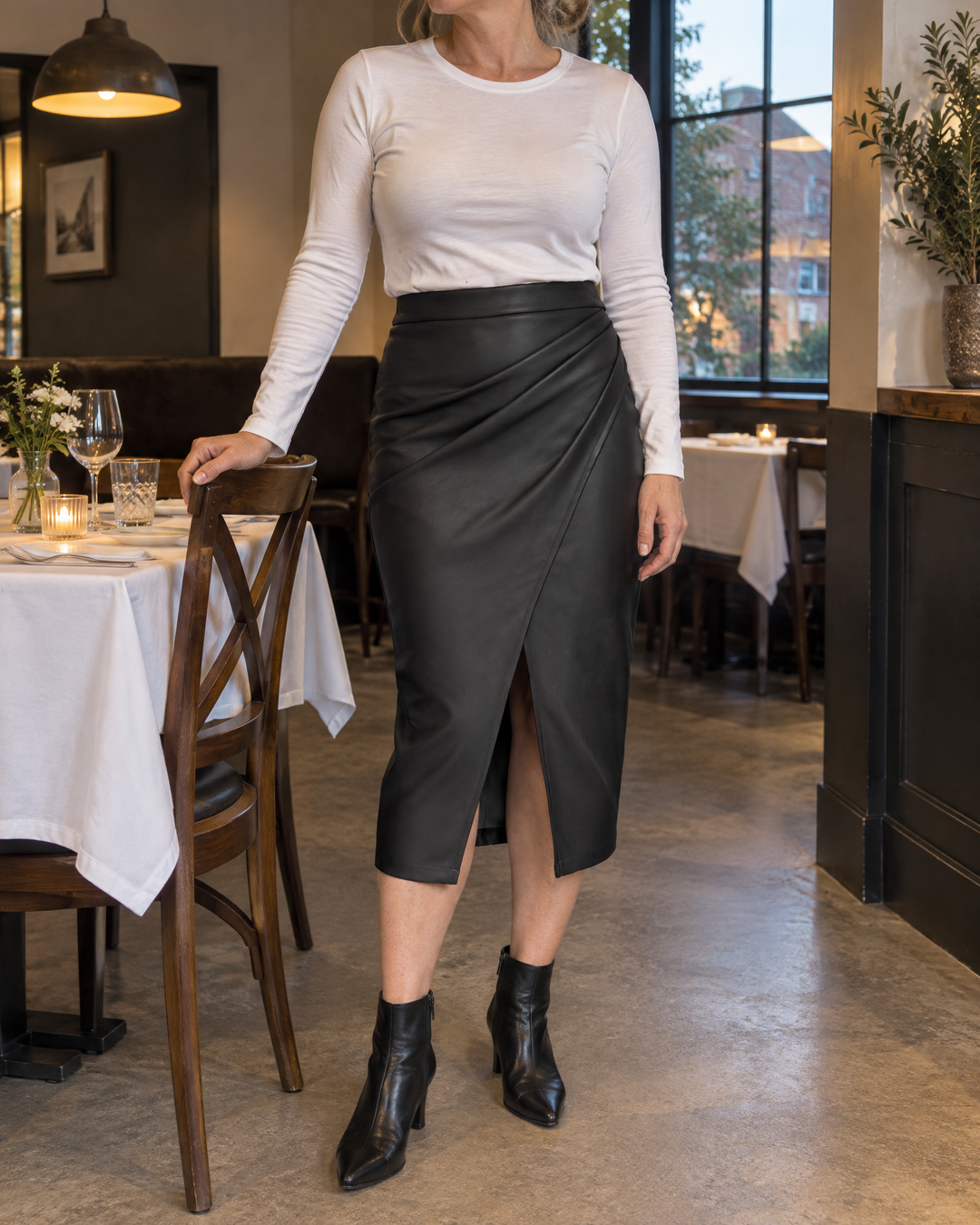 Nadine - Faux Leather Wrap Midi Skirt in black, at a restaurant table in the evening