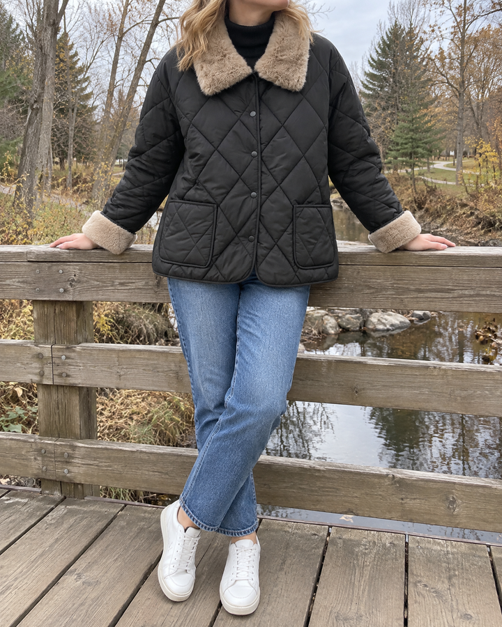 Claire - Faux Fur Collar Quilted Jacket in black, on a footbridge in the park on a cloudy afternoon
