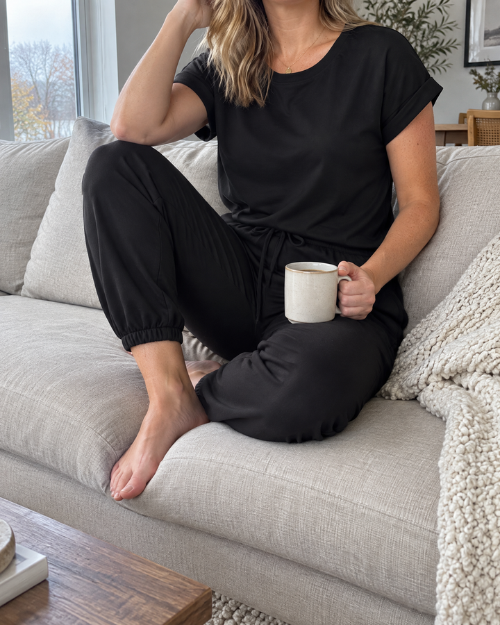 Romy - Tee and Cuffed Jogger Set in black, at home on the sofa on a grey morning